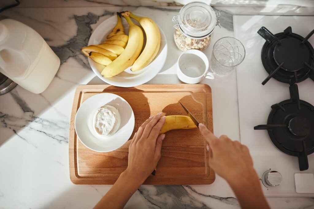 A woman prepares breakfast by cutting a banana for a healthy breakfast dish 