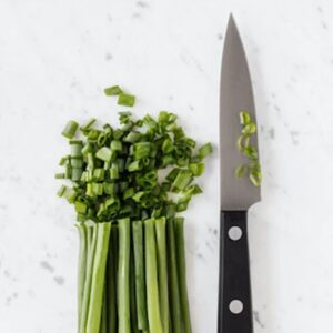 A chefs knife laid next to chopped up green onions 